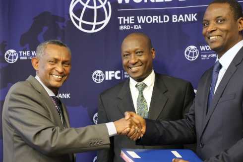 Image shows three men smiling and shaking hands, there is world bank printed on the banner behind the men